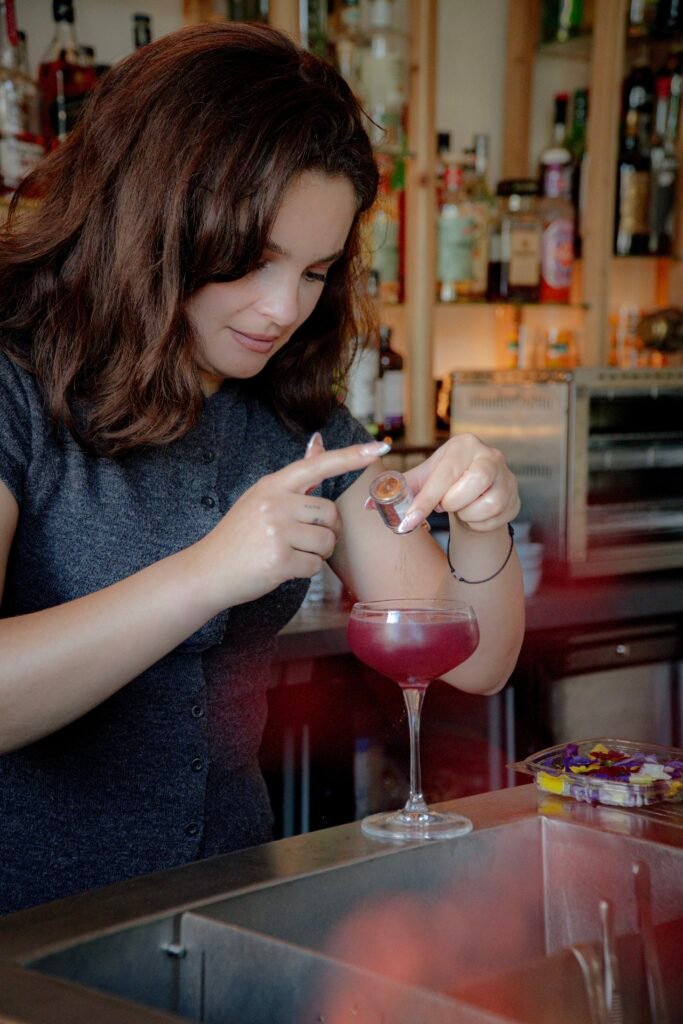 Barman saupoudrant des paillettes sur un cocktail violet dans un verre à pied.