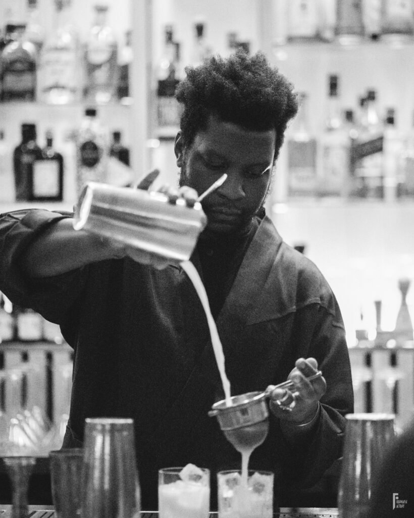 Barman versant un cocktail à travers une passoire depuis un shaker dans un verre avec de la glace.