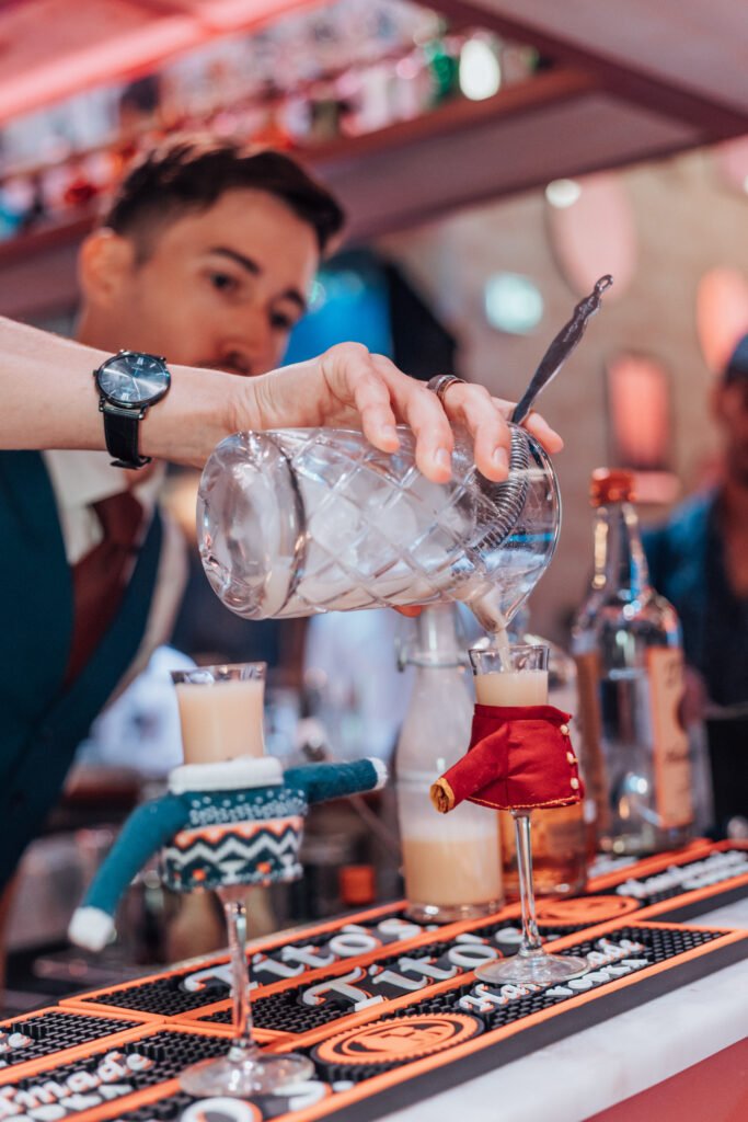 Barman versant un cocktail crémeux dans des verres décorés avec des miniatures de vêtements.
