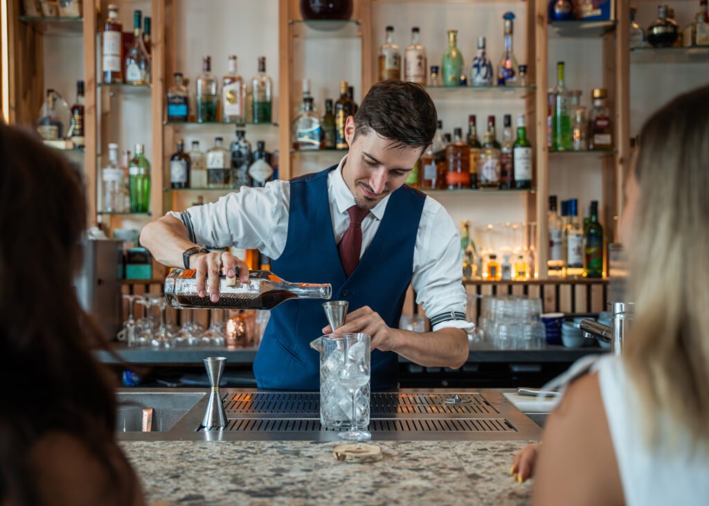 Barman versant du liquide d'une bouteille dans un jigger devant des clients.