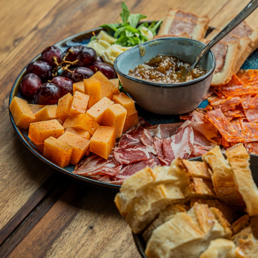 Planche de charcuterie, cubes de fromage, raisins et morceaux de pain.