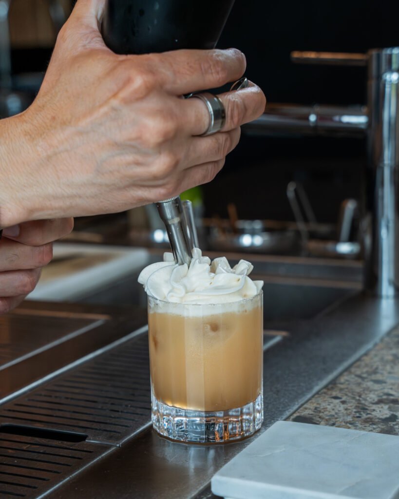 Barman ajoutant de la crème fouettée sur un cocktail au comptoir.