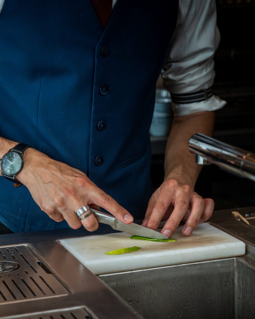 Un barman découpe un agrume sur une planche à découper au bar.