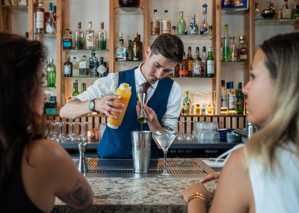Un barman prépare un cocktail au comptoir devant des clients.