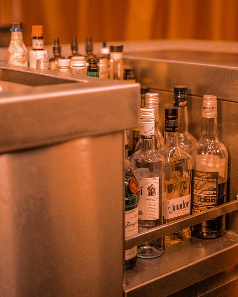 Bouteilles de spiritueux et sirops alignées dans le compartiment de préparation d'un bar à cocktails.