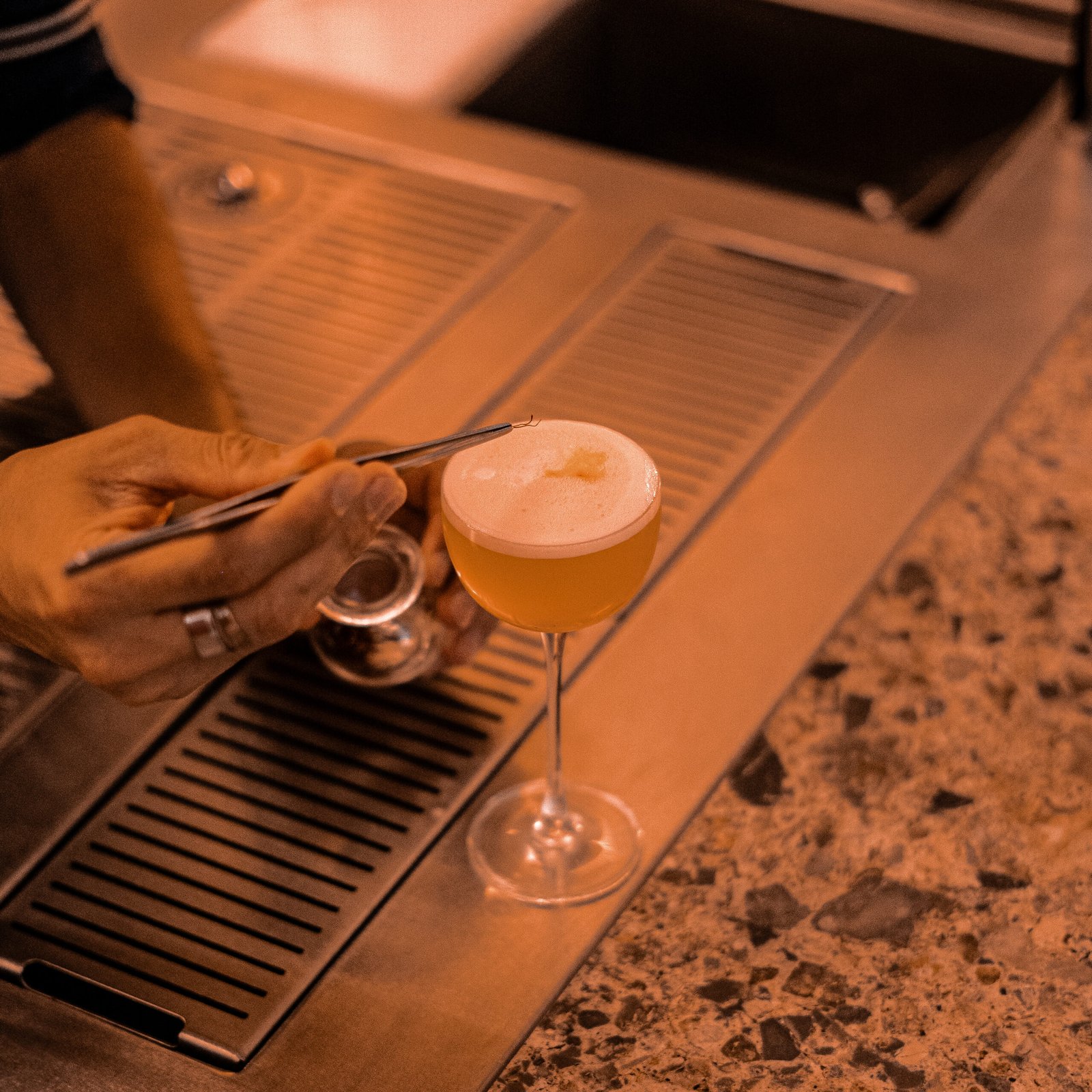 Un barman posant une garniture sur un cocktail mousseux dans un verre à pied.
