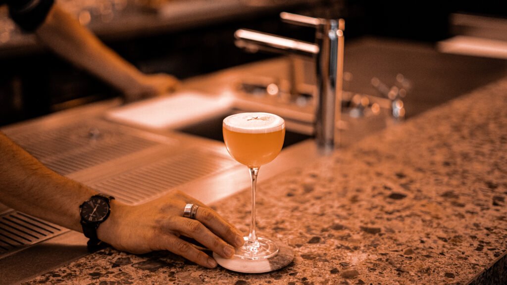 Main d'un barman posant un verre de cocktail mousseux sur le comptoir.