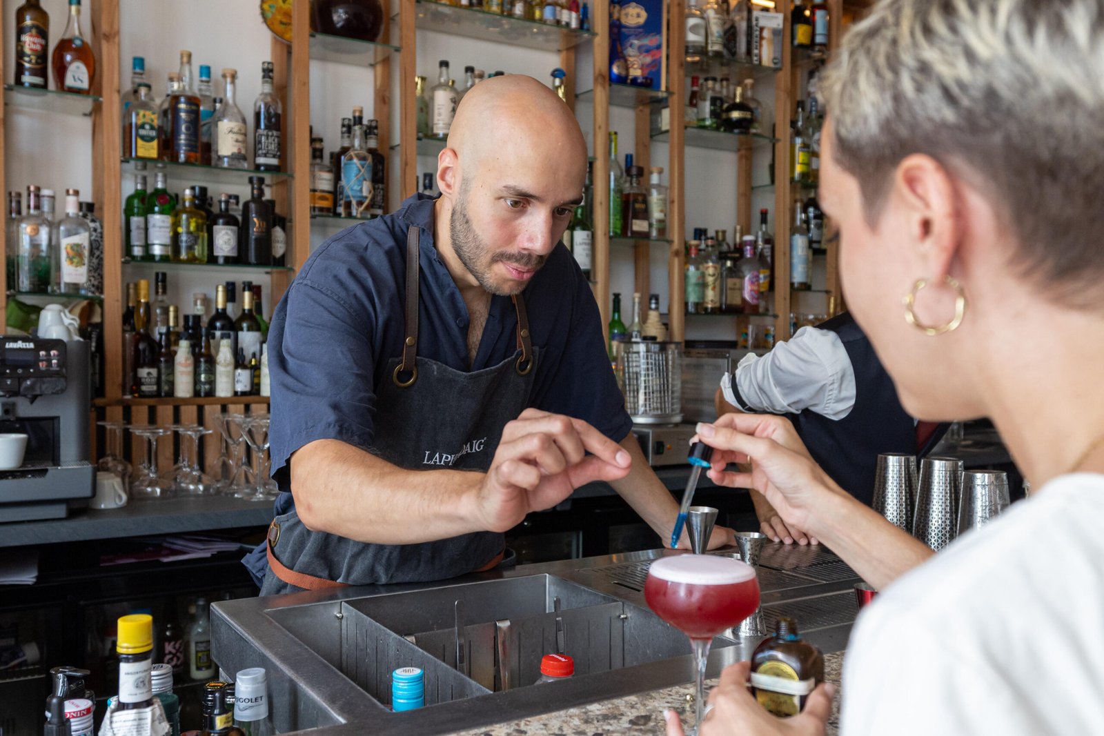 Un barman encadre une cliente qui utilise une pipette sur un cocktail au comptoir.
