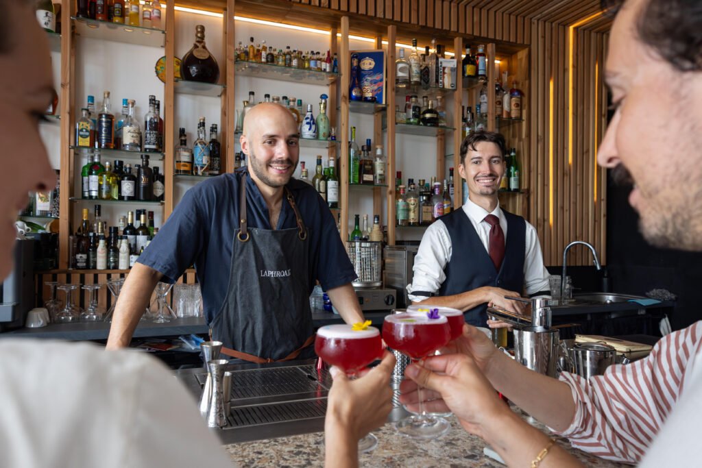 Barmans et clients trinquant avec des cocktails décorés de fleurs au comptoir d'un bar.