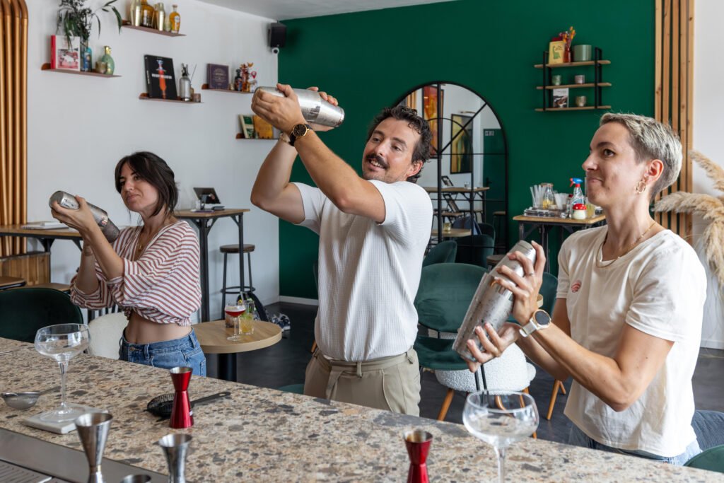 Trois participants secouent un shaker lors d'un atelier cocktail à l'intérieur d'un bar.