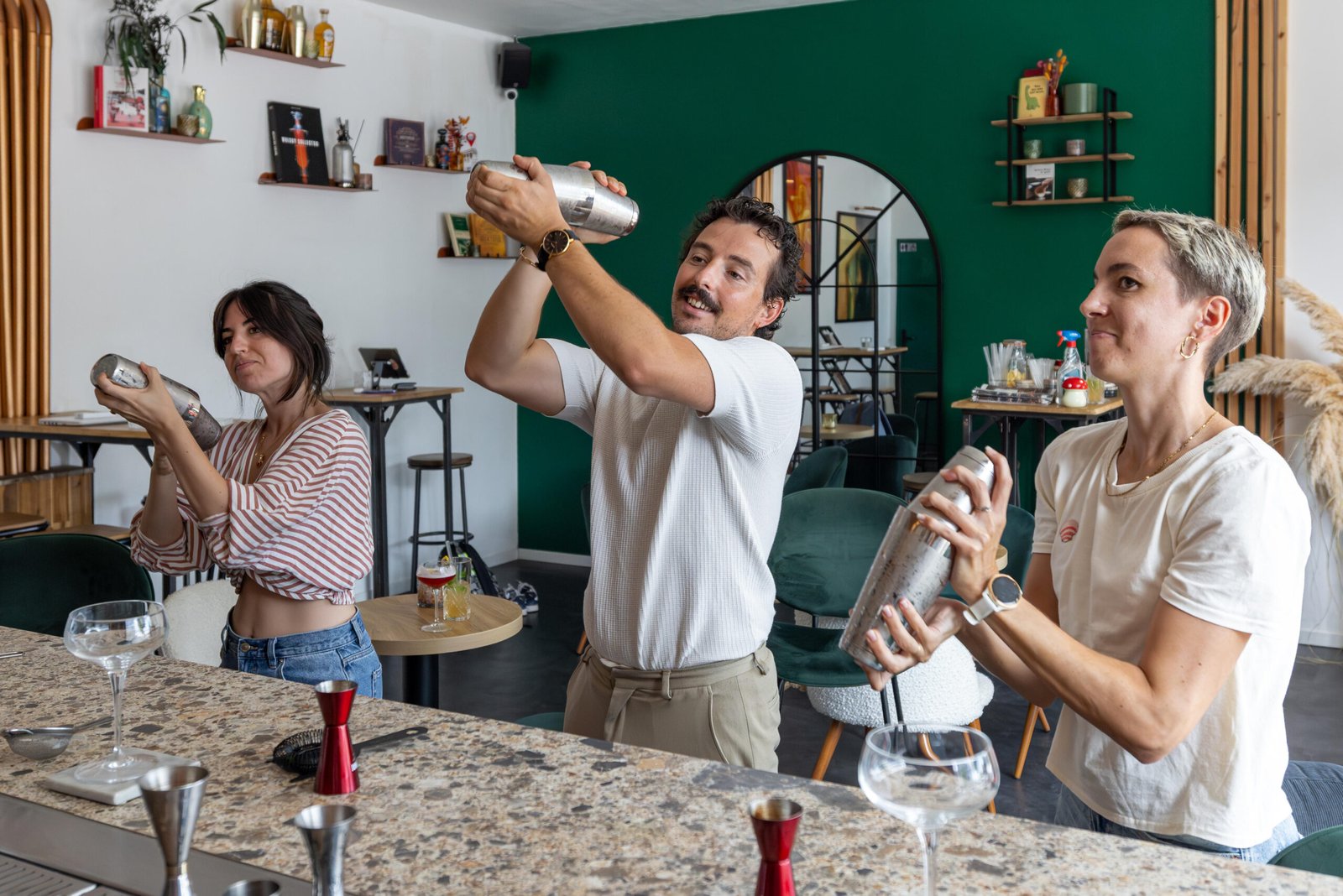 Trois participants secouent un shaker lors d'un atelier cocktail à l'intérieur d'un bar.