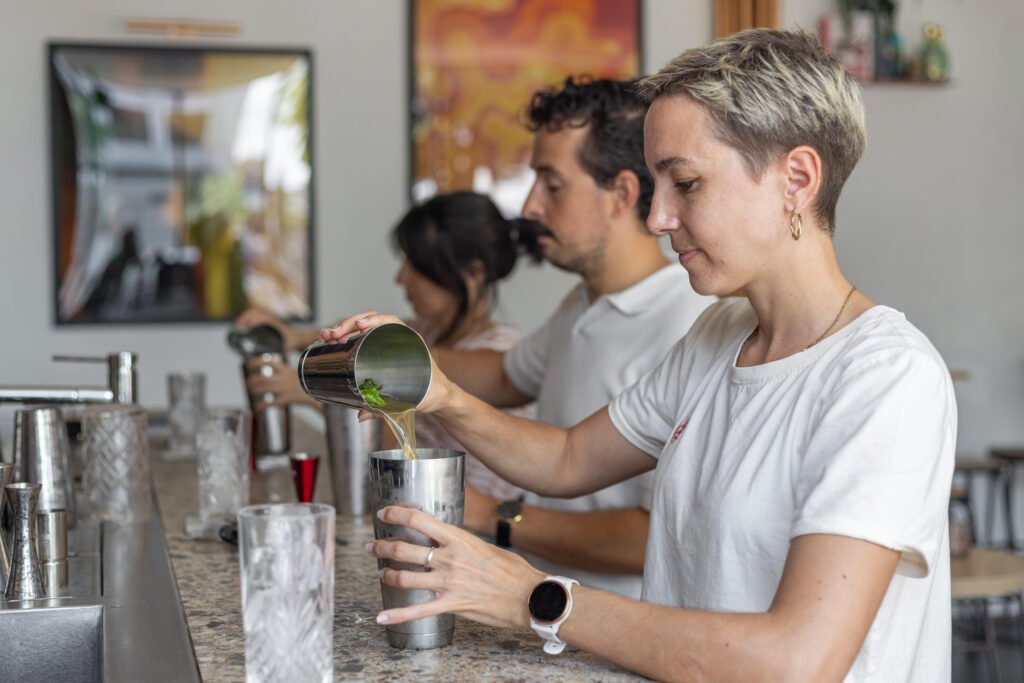 Des participants versent du liquide d'un shaker dans un verre lors d'un atelier cocktail.