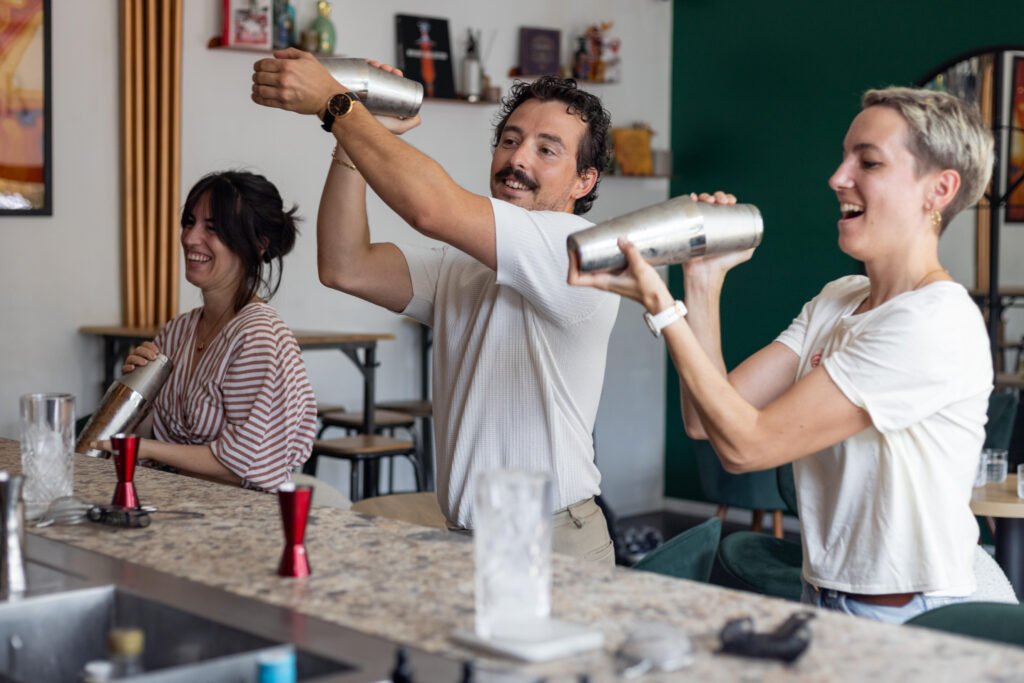 Participants souriants secouant des shakers en métal derrière un comptoir de bar.