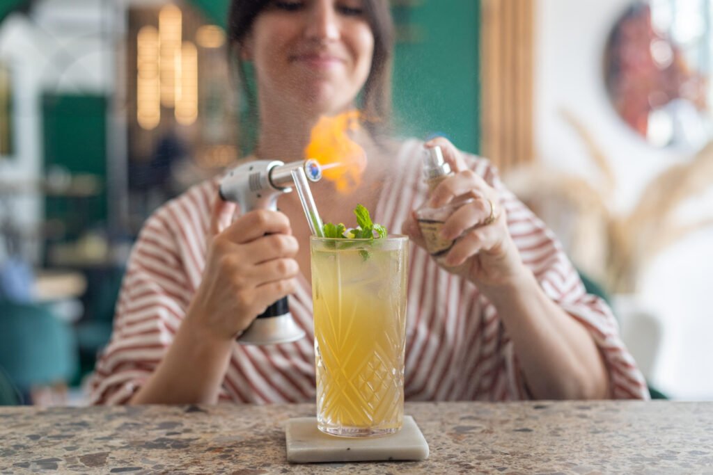 Utilisation d'un chalumeau pour flamber un cocktail garni de menthe sur un comptoir.